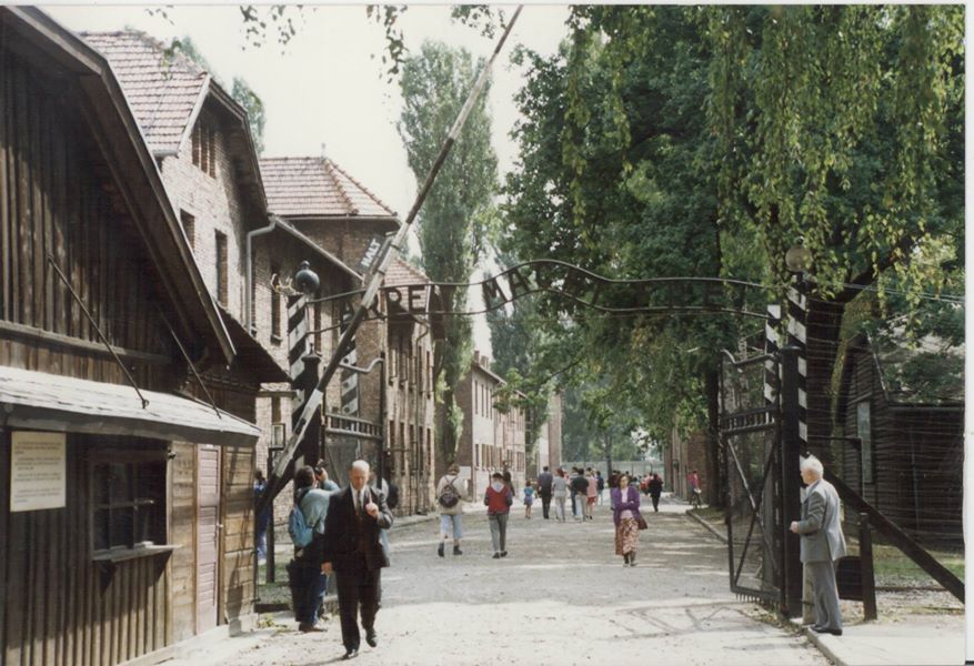 At the Gates to Hell. Pictured at the entrance gates to Auschwitz are Romuald (far right), and Journalist Malcolm R Fane seen walking (far left).
