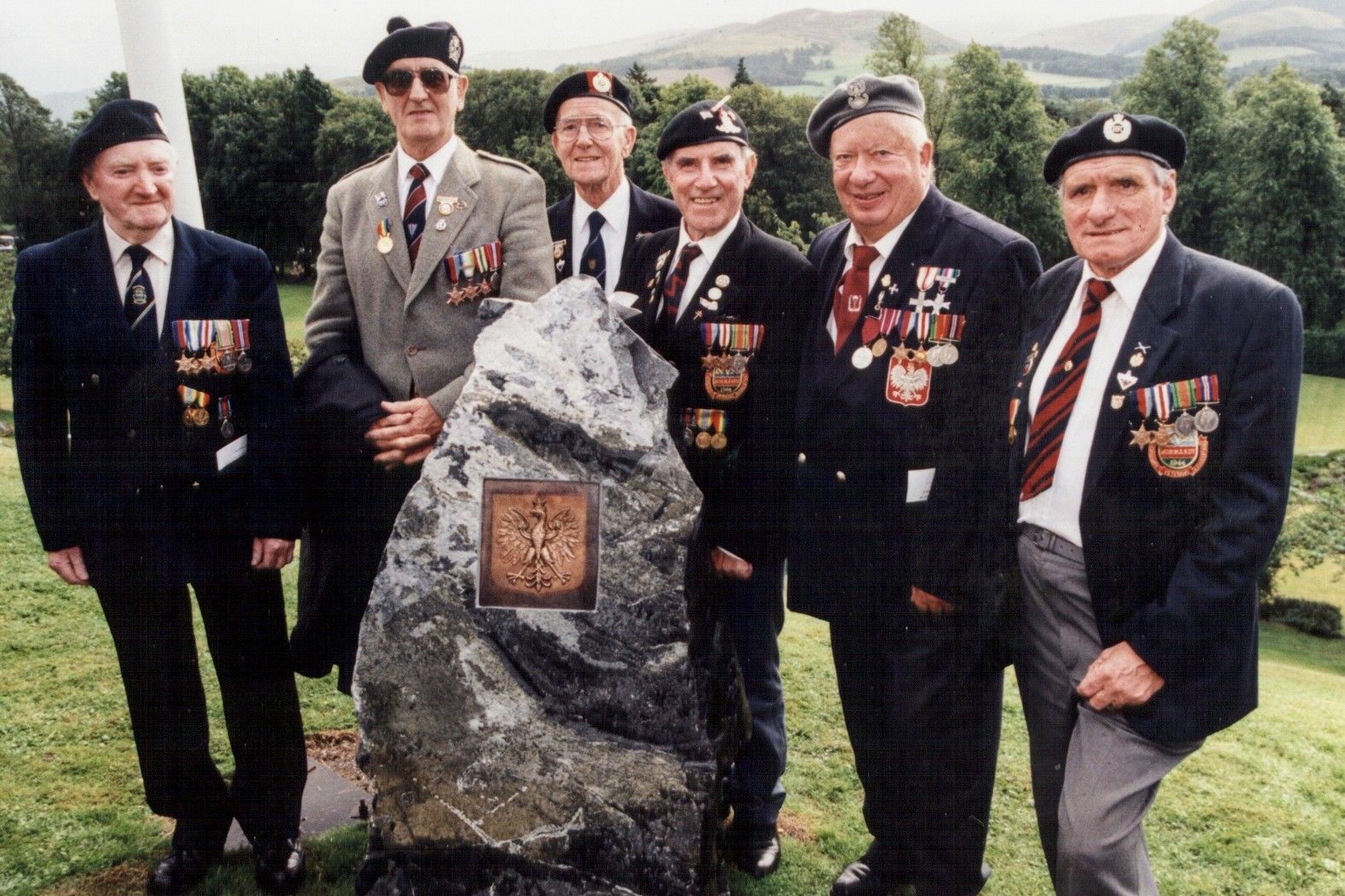 Polish Ex-Combatants group around the tri-stone memorial graced with a bronze emblem of Poland's crowned eagle.